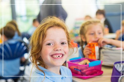 young girl eating a packed lunch at a table with friends at school