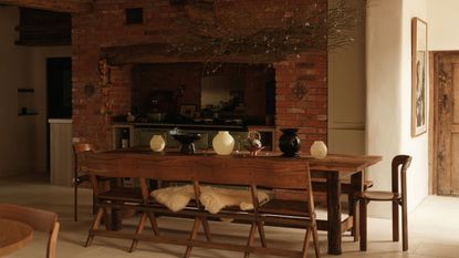 A dining area with an oak dining table in the middle and different table top accessories including bowls and vases. Above the dining table is large hanging pendant light 