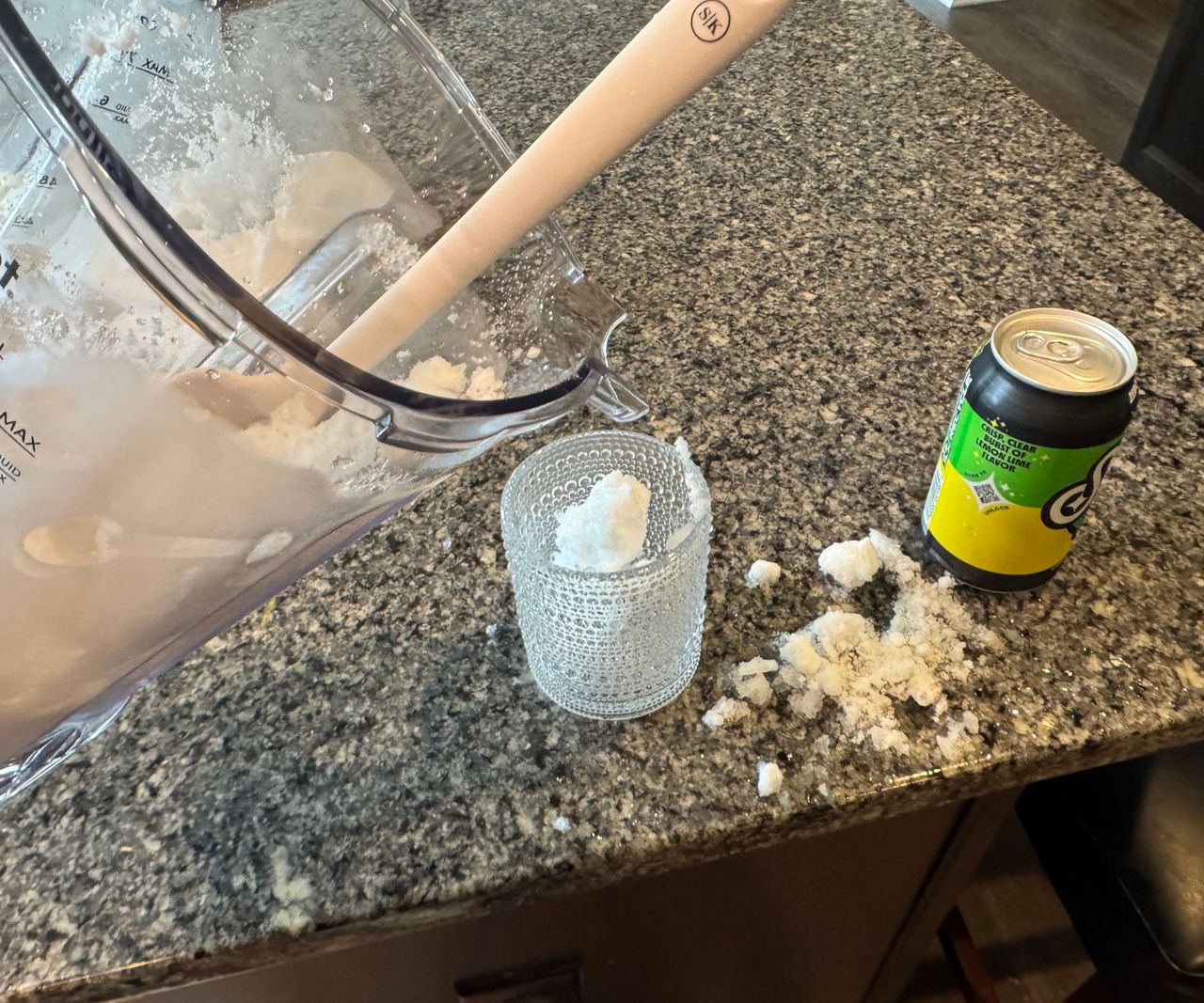 Ice being poured from a clear blender pitcher into a glass, and spiling onto the counter.