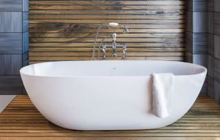 a white bath in a grey tile and timber cladding bathroom