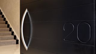 Modern dark wood front door with metal handle and house number etched beside it