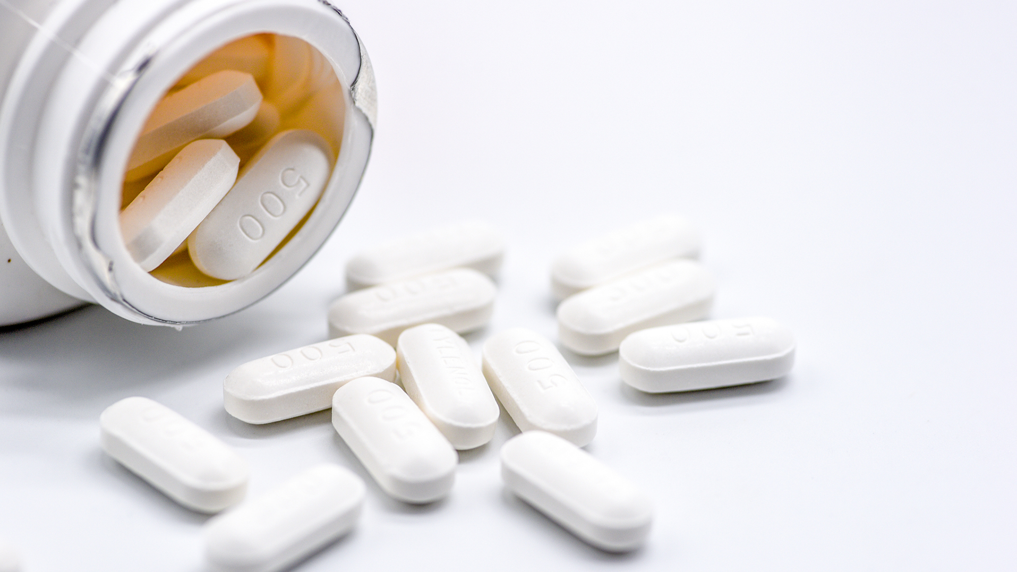 A close up of an open white bottle on its side with large white pills coming out