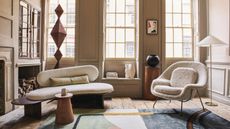 Living room with wooden floor and panelled walls, three large sash windows with wooden shutters, sculptural vases and items on display.