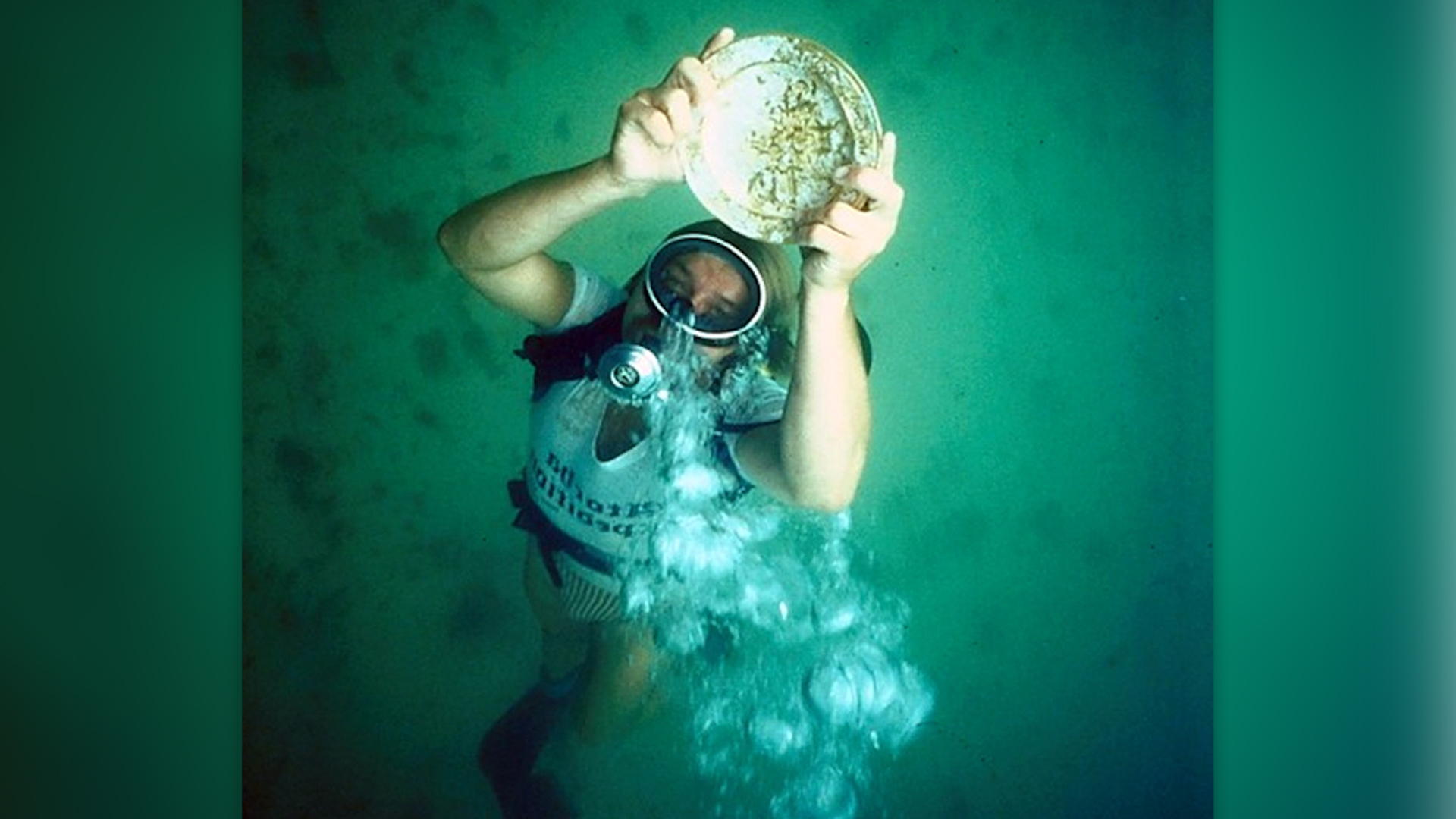 We see a diver holding a metal plate and swimming upward, with bubble coming out of their mouth.