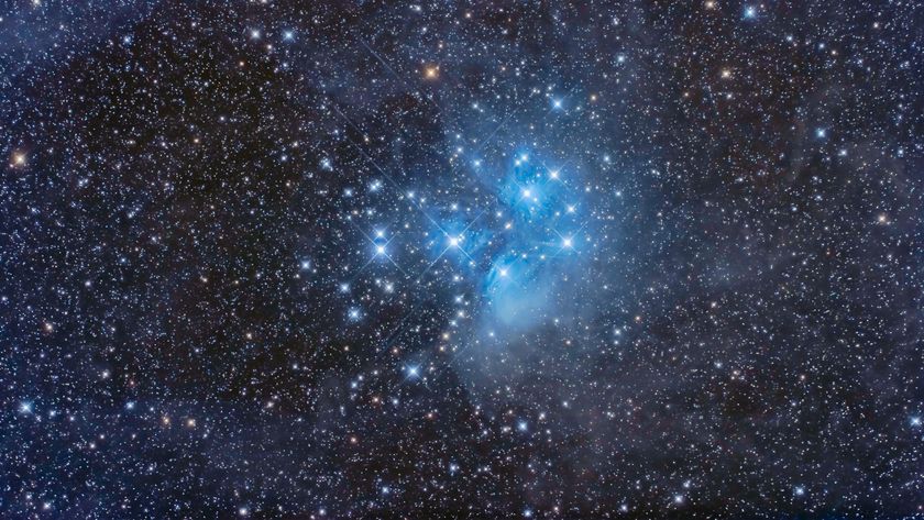 A collection of bright blue-white stars can be seen shining bright against a more distant multicoloured starfield.