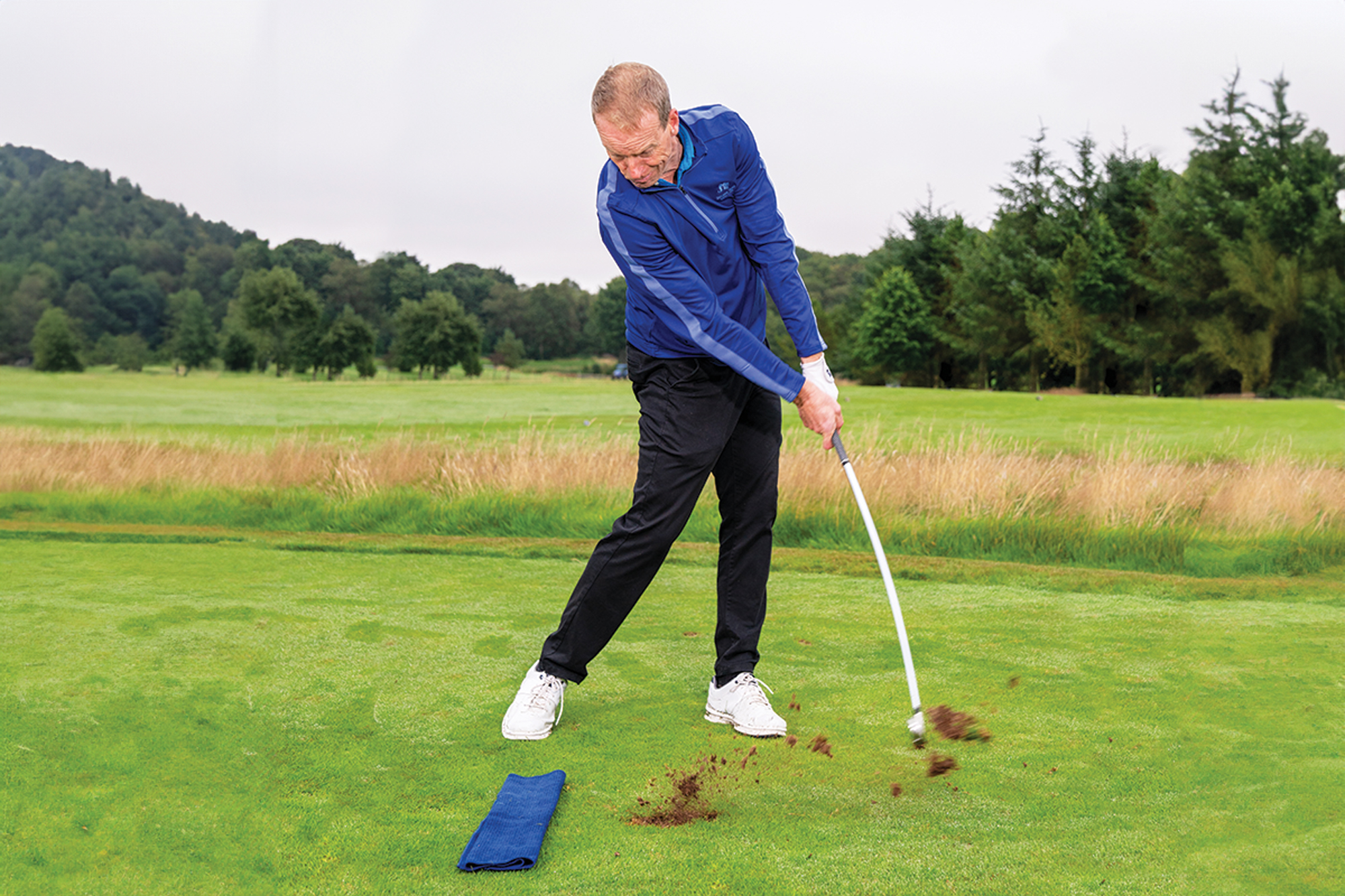 Neil Marr demonstrating a ball striking drill, by placing a towel on the ground behind the golf ball, and taking an iron shot with a divot past the towel to avoid fat contact
