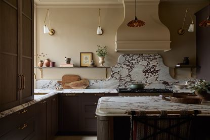 A dark kitchen with a dramatically veined countertop and curves. Lots of decorative elements such as wall lights and shapely details.