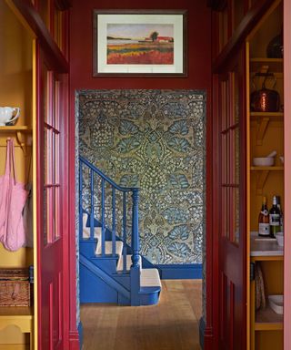 blue hallway with blue banister and patterned wallpaper and red kitchen doors
