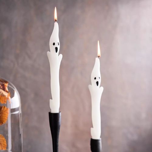 White tapered candles in the shape of ghosts, on black candle holders