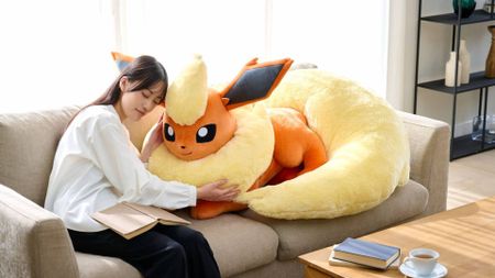 Marketing image of a person cuddling a Pokedex-size Flareon plushie.