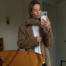 Anouk wears a beige wool jacket, white top and large beige tote bag.