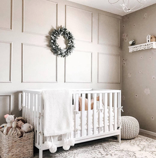 A neutral nursery with wall panelling and wallpaper in soft beige, with a white crib.