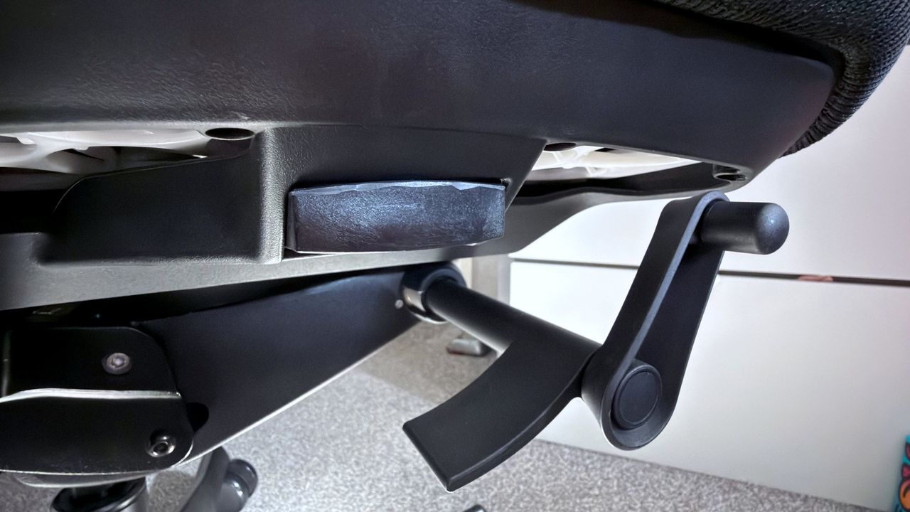 A photo of an Autonomous ErgoChair Ultra 2, showing a close-up view of the tension wheel for the back recline mechanism and latch to adjust the seat height