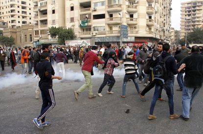 Supporters of the Muslim Brotherhood run for cover from a tear gas cannister during clashes with riot police following a protest in Cairo on December 20, 2013. 