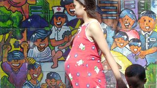 a pregnant woman wearing a pink dress walks by a colorful mural with her son holding her hand