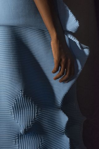 A close up of a the pleats of a sculptural Issey Miyake dress with woman’s hand