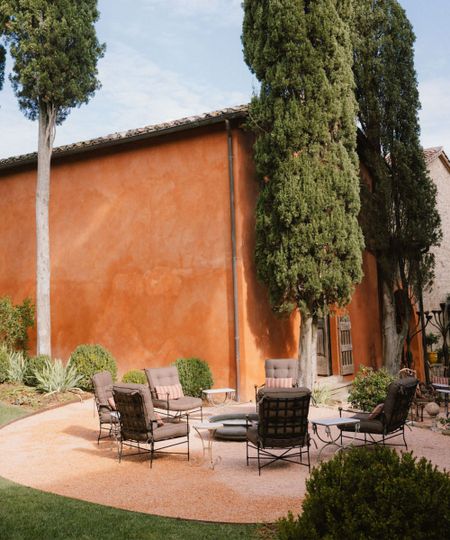 Italian terrace with teraccotta painted building surrounded by trees, plants. Seating area on stone patio sat around firepit