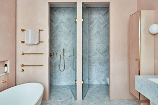A pink bathroom with a white bath and a walk-in shower with gold hardware