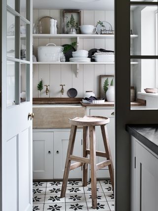 a nordic-style house with open white kitchen shelves, a black and white patterned tile floor, and a wooden stool