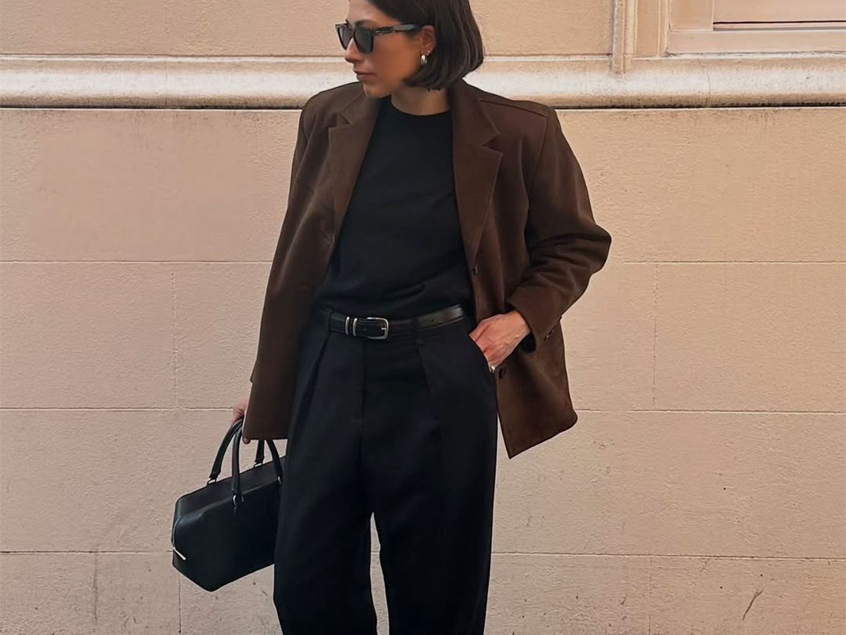 Influencer Lucy Alston wears black trousers, a black tee, and a brown suede blazer.