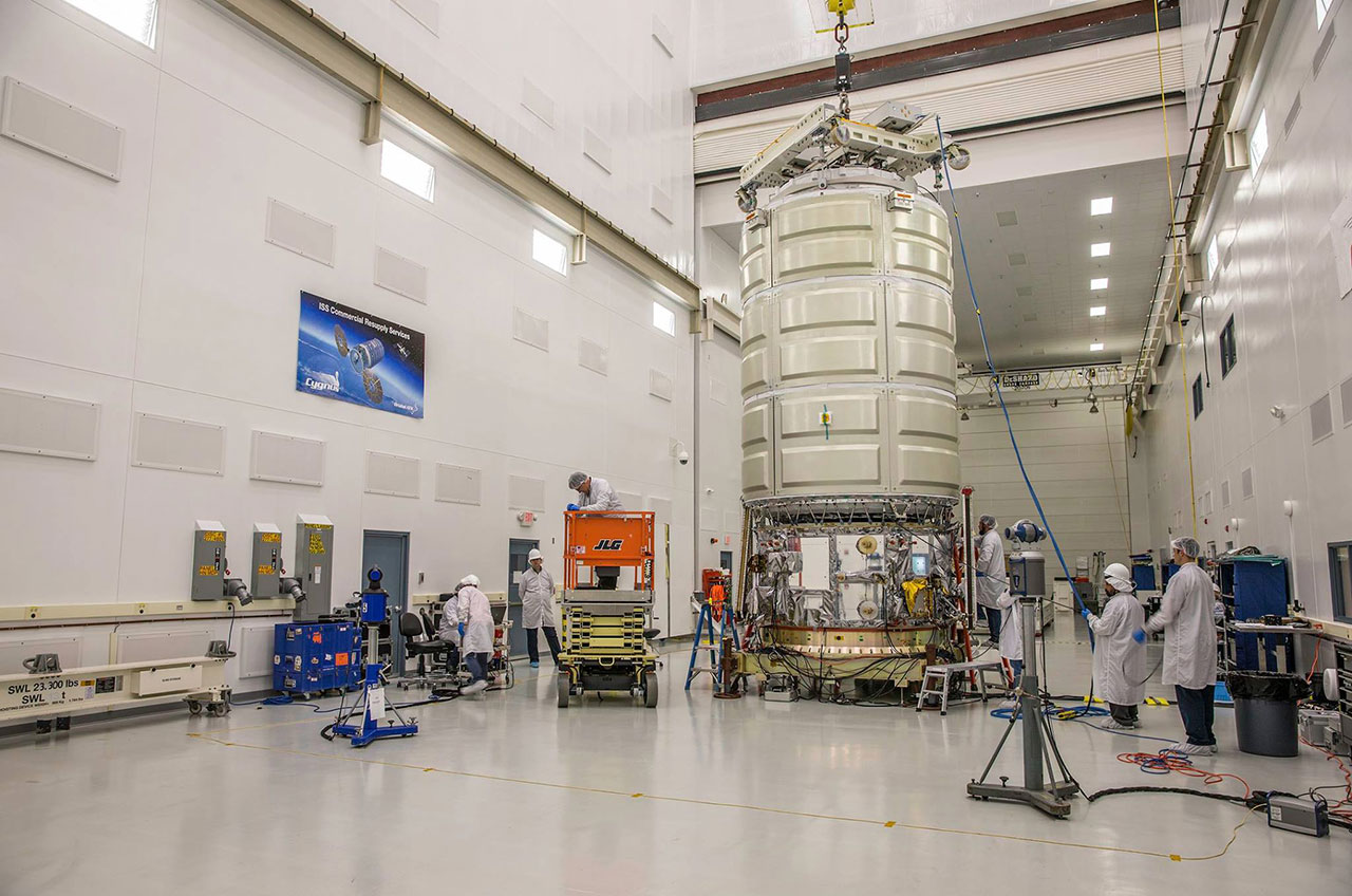 A large, cylindrical spacecraft stands upright in a large room