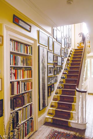 A hallway in a period property with yellow painted staircase and home library shelf