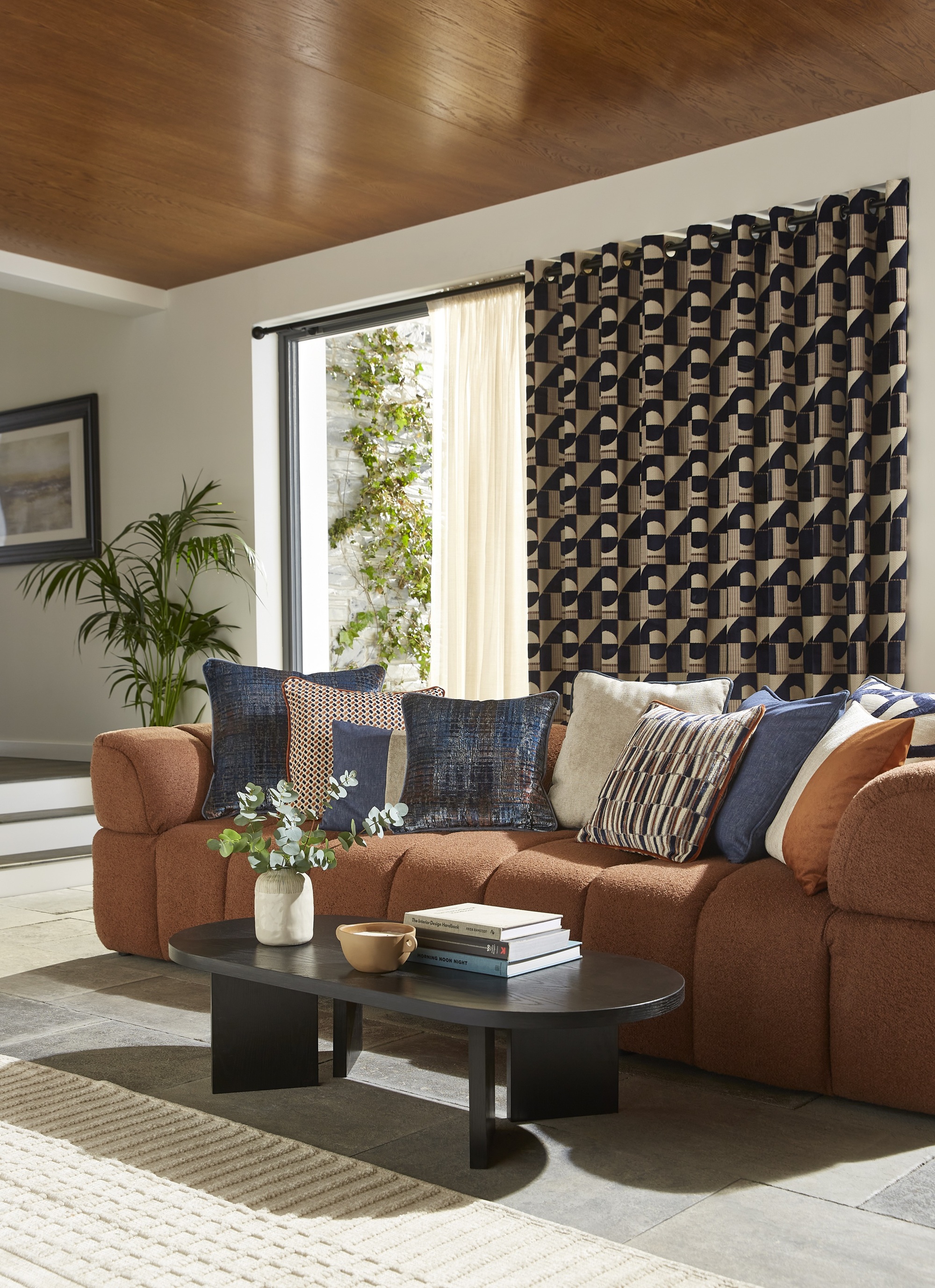 an orange sofa in a living room with a wooden ceiling and patterned curtains