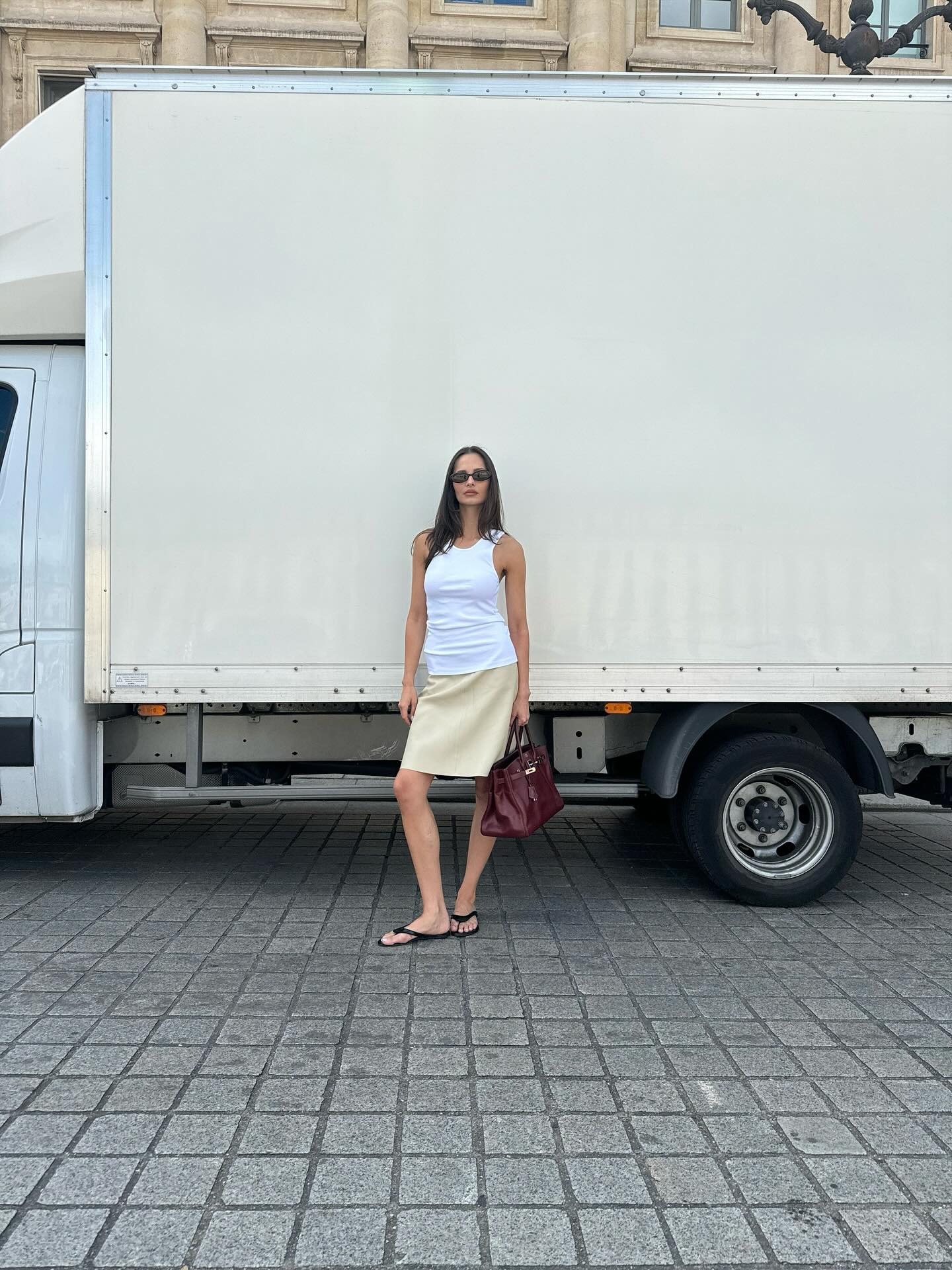 Pia Mance wearing a white tank top, cream knee-length skirt, and flip-flops.