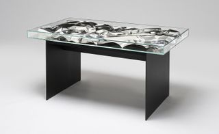 Table with black base and a top with crushed aluminium in a glass case