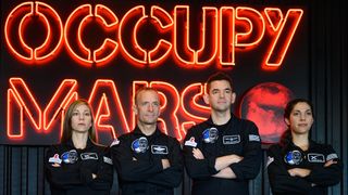The Polaris Dawn crew. stand in front of large neon red letters spelling out "occupy Mars"