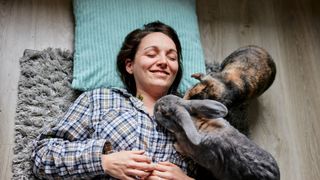 Woman lying down on the floor and teal cushion with two rabbits on top of her