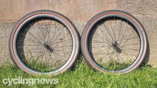 A pair of black wheels with tanwall tyres leant against a pebledash wall on some grass