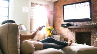 Woman sitting on coach with her feet up pointing remote at TV