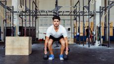 A man performing suitcase deadlifts with dumbbells at a crossfit gym