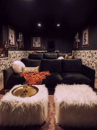 movie room with velvet couches, wallpaper, black walls and ceiling, fluffy footstools, tray, prints on walls, wall lights