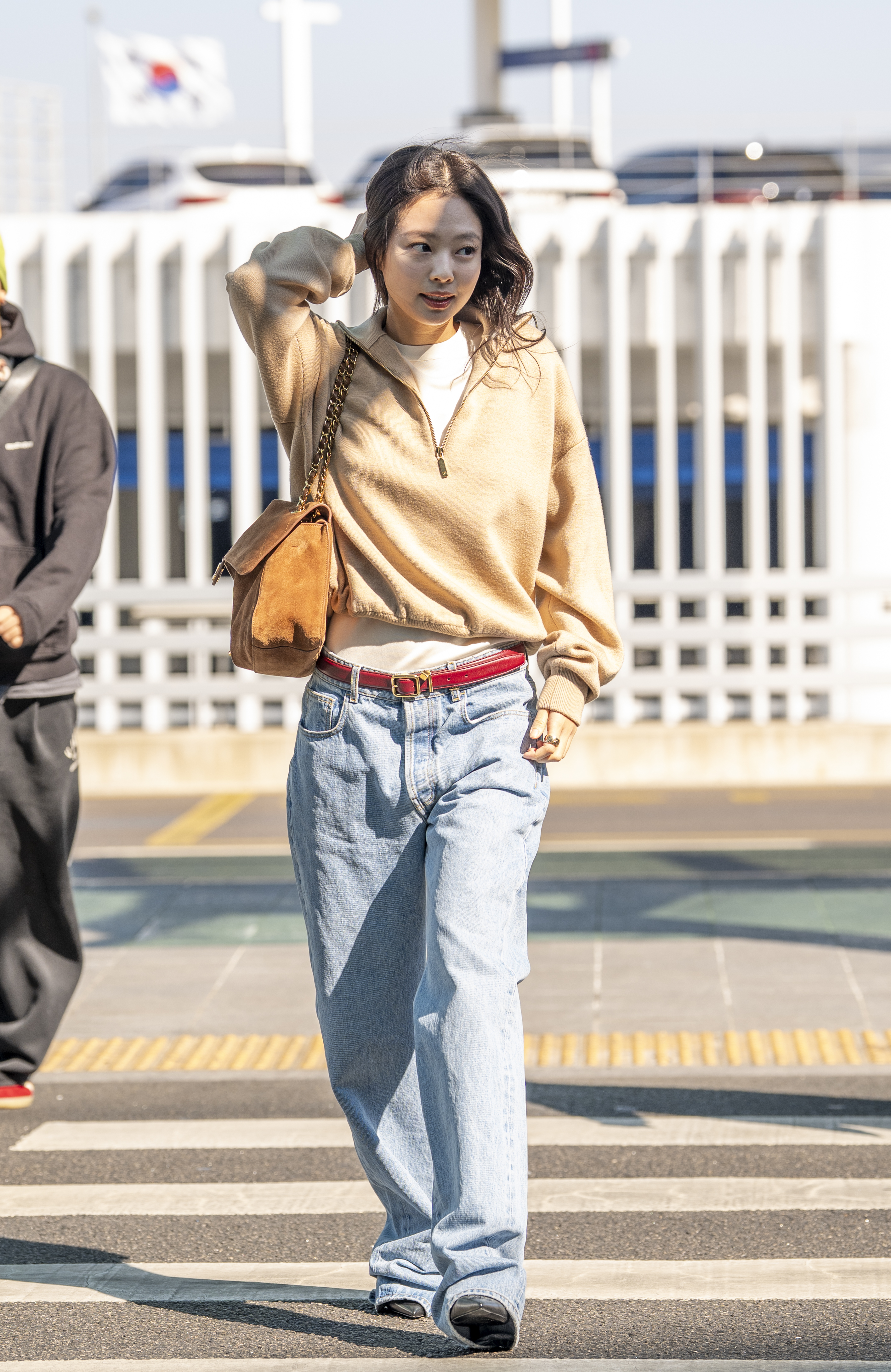 An image of Jennie Kim at the airport wearing the Chanel quarter-zip sweater, bagg jeans, ballet flats and a suede bag.