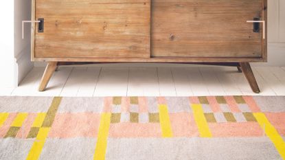Pastel colored patterned rug in a hallway in front of a wooden cabinet to support a guide for how to clean a rug at home