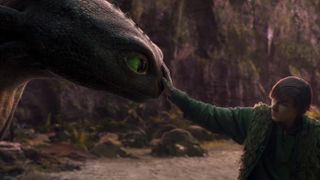 a boy touches a black dragon with green eyes in a still from the live action how to train your dragon