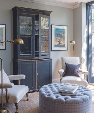 A blue cabinet in a living room with a foot stool and a gold lamp