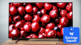 The LG B6 OLED TV displaying a high-contrast, close-up image of dark red-colored cherries. Next to the TV is a superimposed badge that reads: "TG Savings Squad".