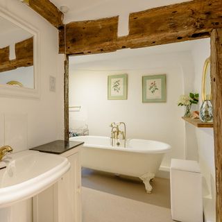an open plan bathroom with exposed timber beams on the entrance, and a white freestanding clawfoot bathtub
