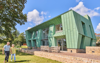 Exterior of green house with brick outdoor patio and lawn in front, with two people holding hands 