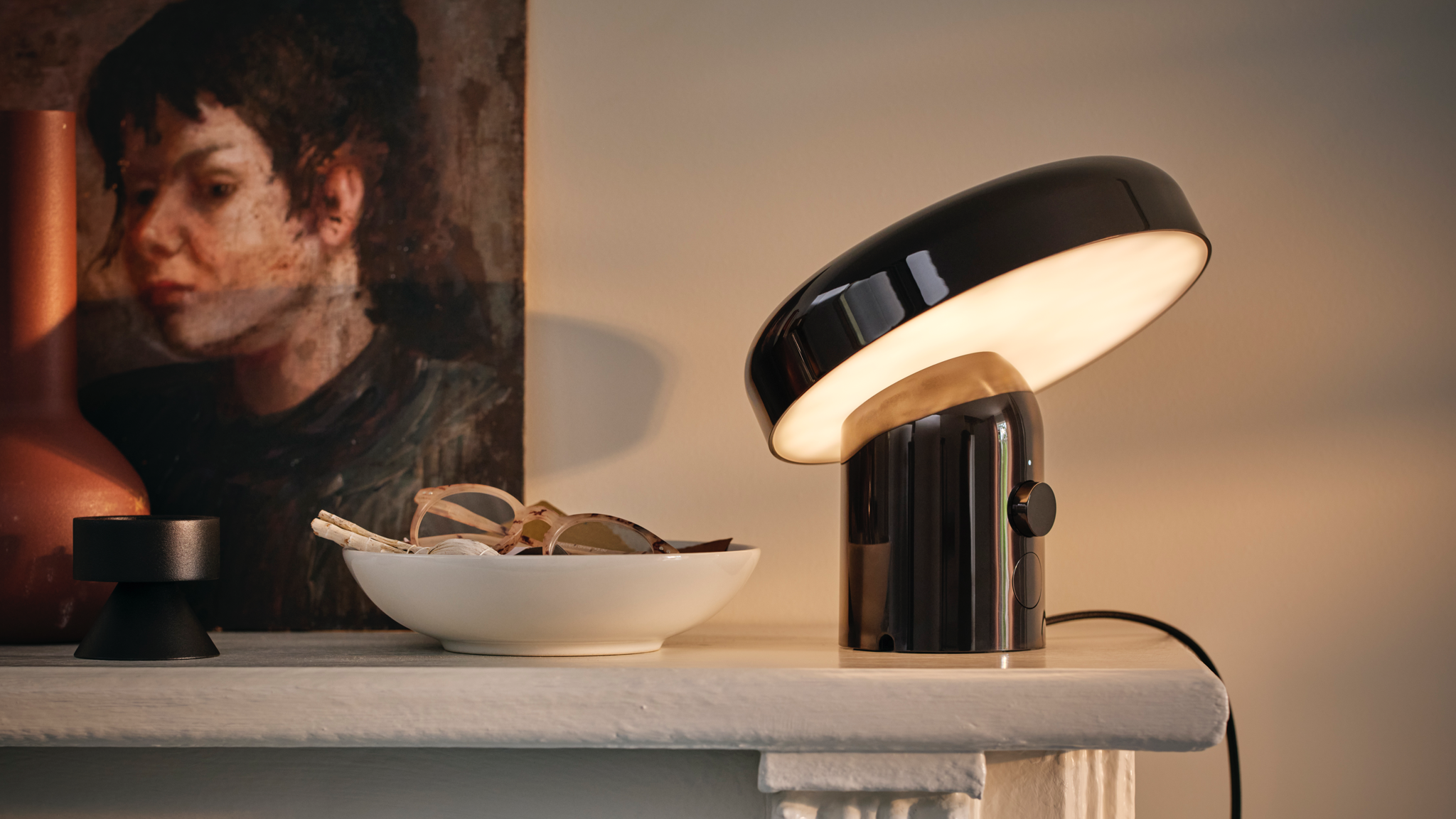 IKEA BLOMPRAKT speaker lamp on a white fireplace with a bowl beside it and a painting on the wall behind it