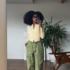 a woman wearing a butter yellow cardigan sweater, green pants, and sunglasses