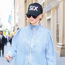 Charlize Theron wearing a denim bomber jacket, white balloon pants, white sneakers, and a baseball cap in NYC