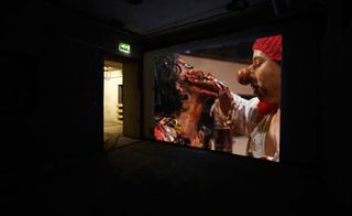Two very dirty-looking pirates are standing face to face. One has a hand over the other one's mouth. The photograph is projected on a concrete wall.