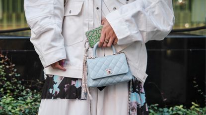 a close-up street style photo of a woman holding a crossbody cell phone bag with a white denim jacket