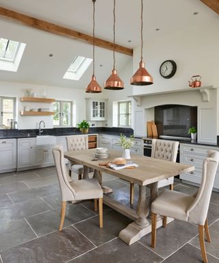 A large kitchen layout idea with skylights, gray cabinetry and copper pendant lighting over a wooden dining table.