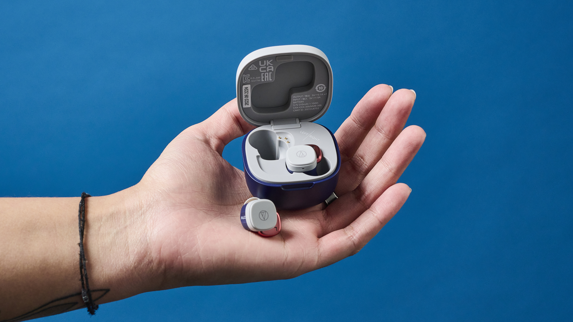 A pair of Audio-Technica ATH-SQ1TW wireless earbuds and their case sitting in the palm of a person's hand