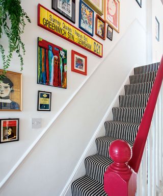 Stairway with white painted walls and red painted handrail, carpeted stairs, colorful picture walll